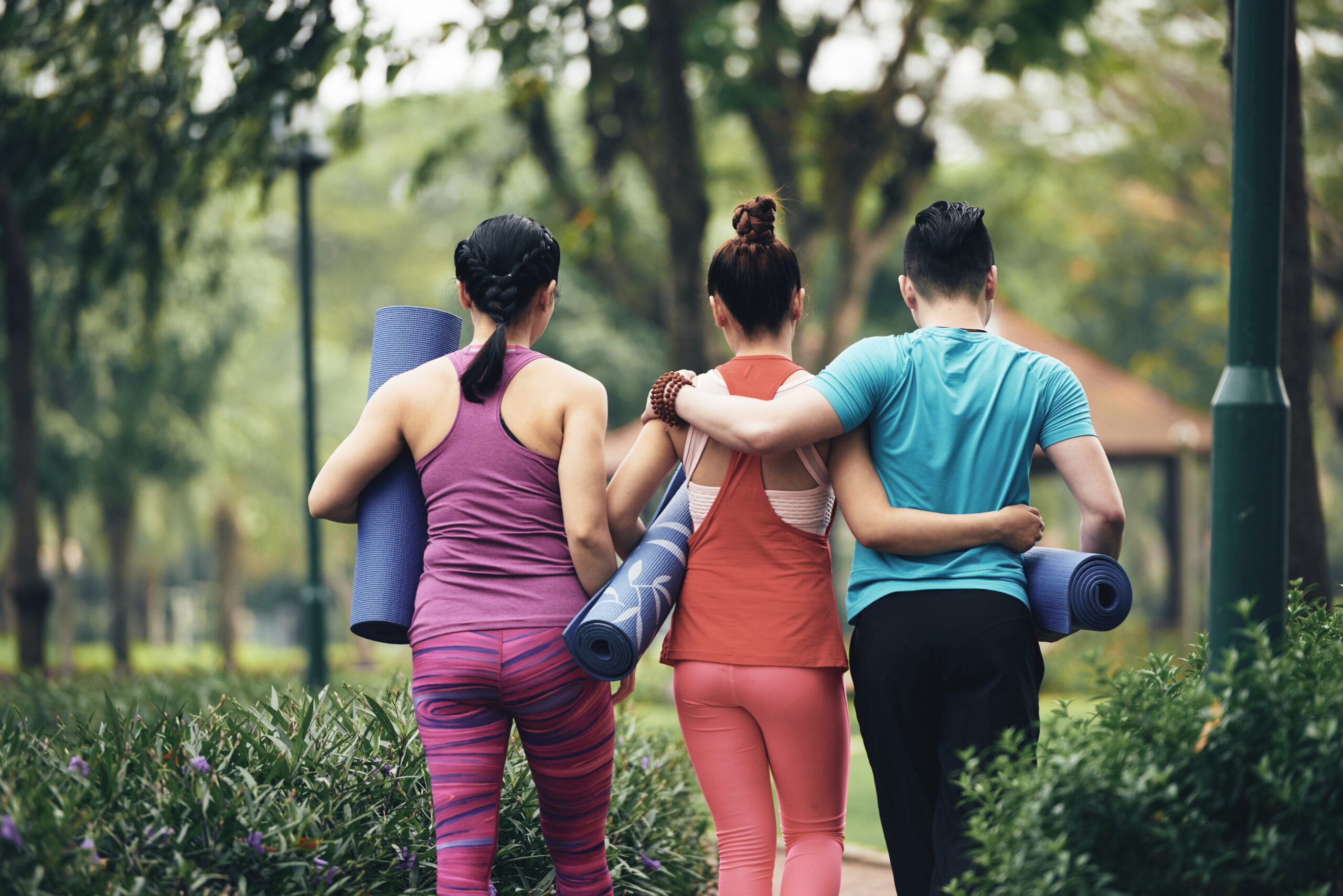 Rear view of young people with yoga mats going to park for practice